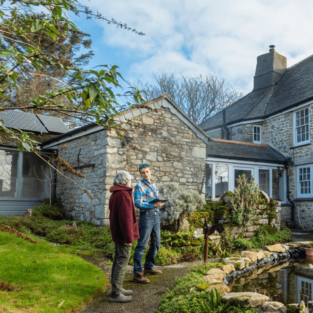 JCS Page discussing a survey with a client outside a traditional Cornish stone farmhouse