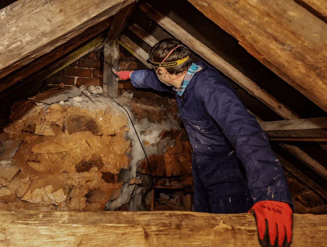Surveyor examining an exposed chimney breast and roof timbers in a loft space